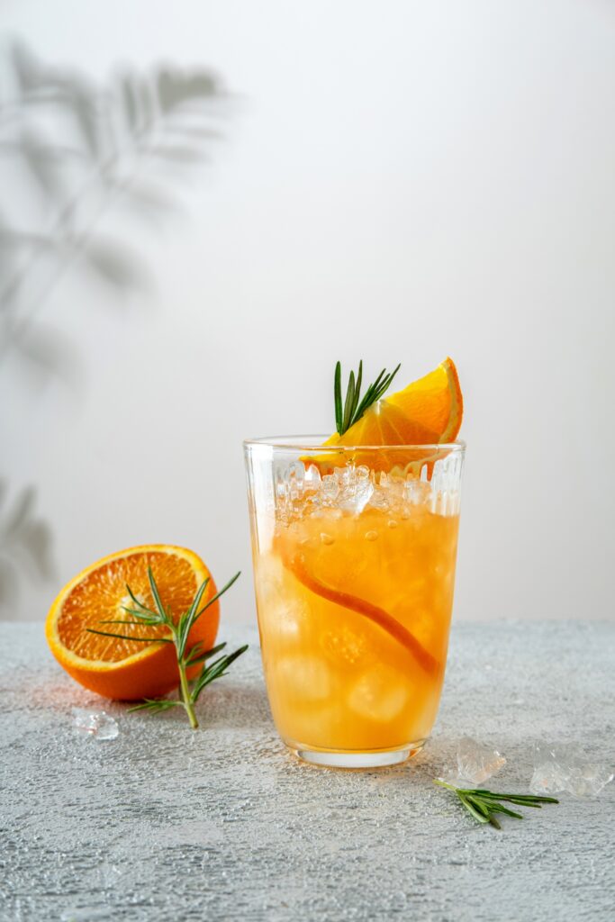 Orange Tonic Drink mit Eis, Orangenscheibe und Rosmarin. 