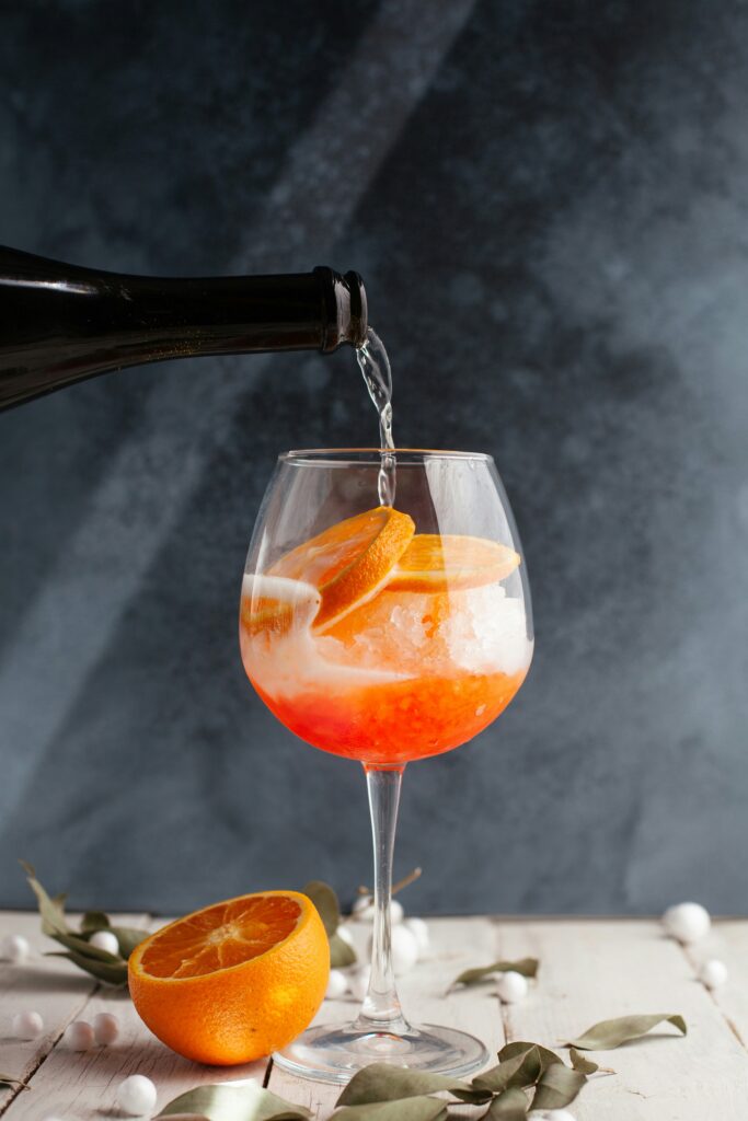 Bauchiges Weinglas mit Orangenscheiben, Eis und Orangendrink. Proseccoflasche gießt frischen Prosecco ein. 