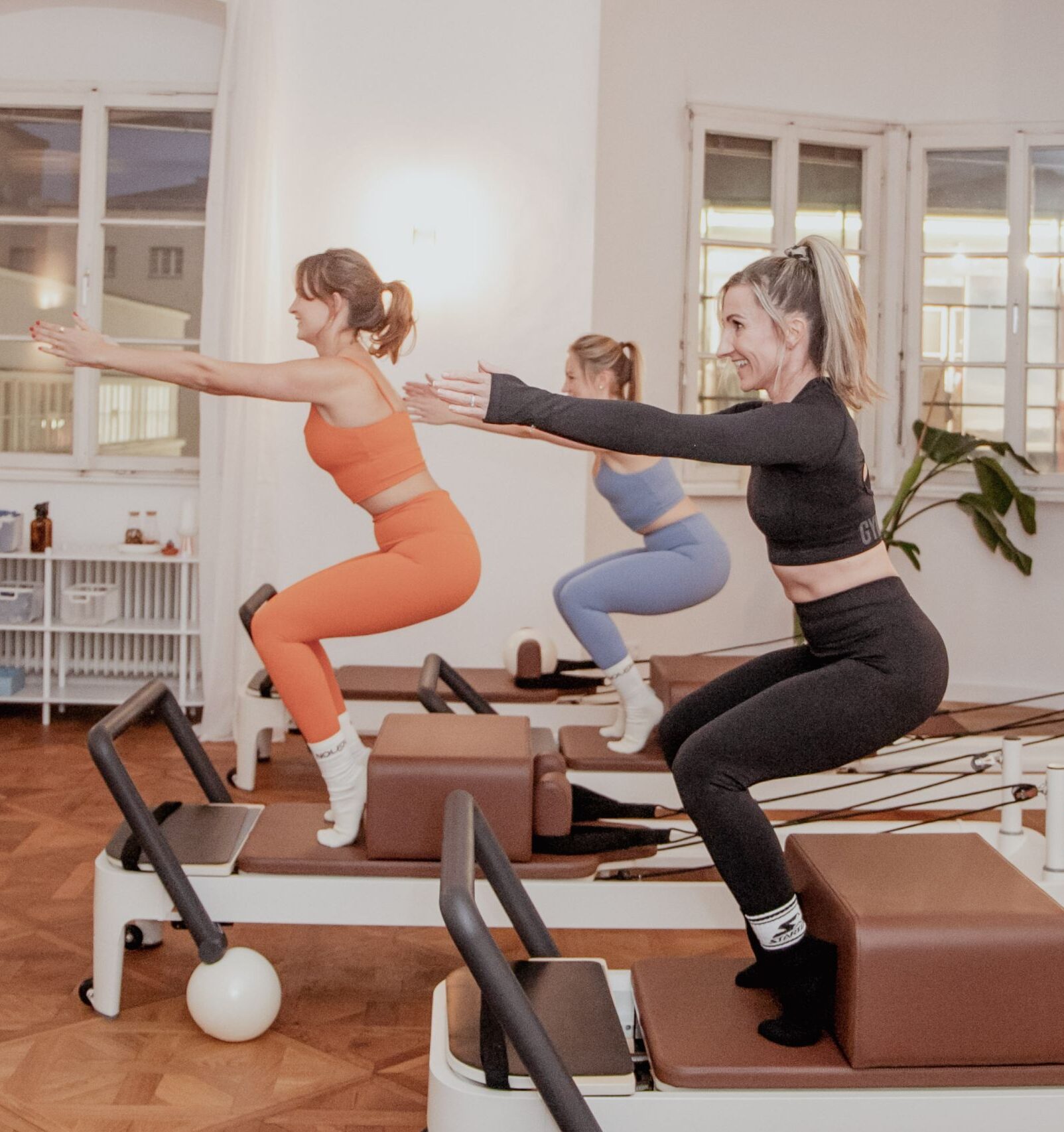 Drei Frauen im Sportdress machen Reformer Pilates.