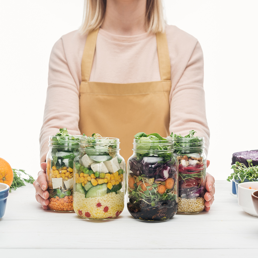 Eine Frau hÃ¤lt 4 Mahlzeiten in SchraubglÃ¤sern: Salate, Bohnen, Quinoa, Mais, Tofu, SchafskÃ¤se â perfektes Meal Prep