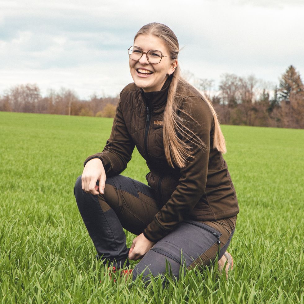Junge Frau kniet in einem Feld Wintergerste.
