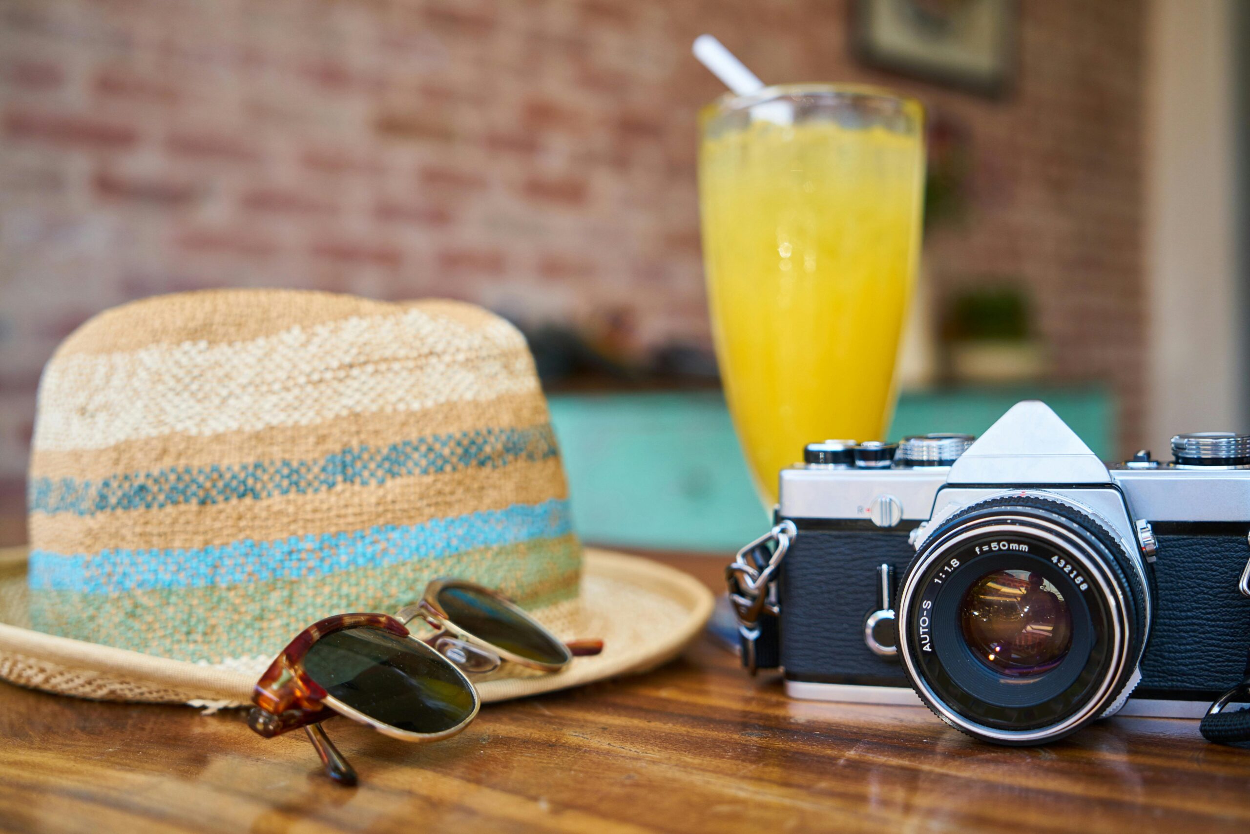 Sonnenhut, Sonnenbrille, Kamera und Getränk auf einem Tisch