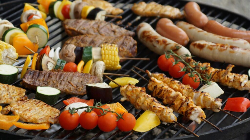Grillrezepte: Nahaufnahme vim Grill auf dem Gemüsespieße, Tomaten, Hähnchenspieße und Würstchen liegen.