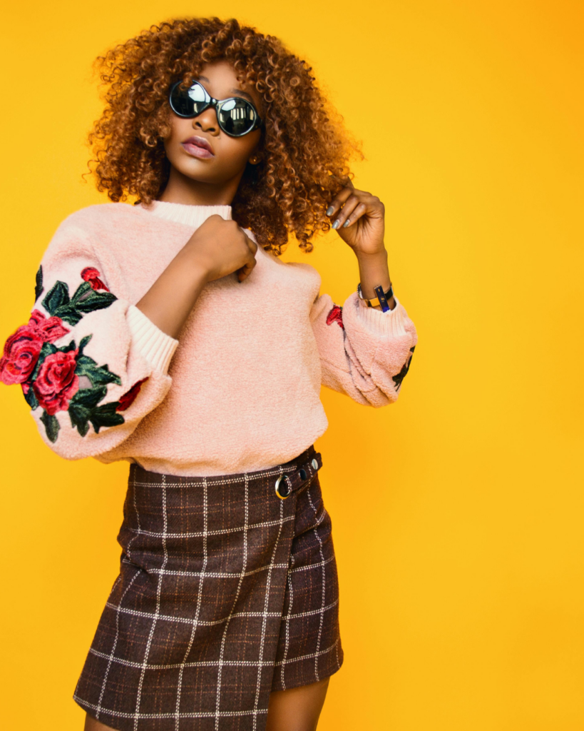 Eine Frau, mit rosa Pulli und Rock vor gelben Hintergrund