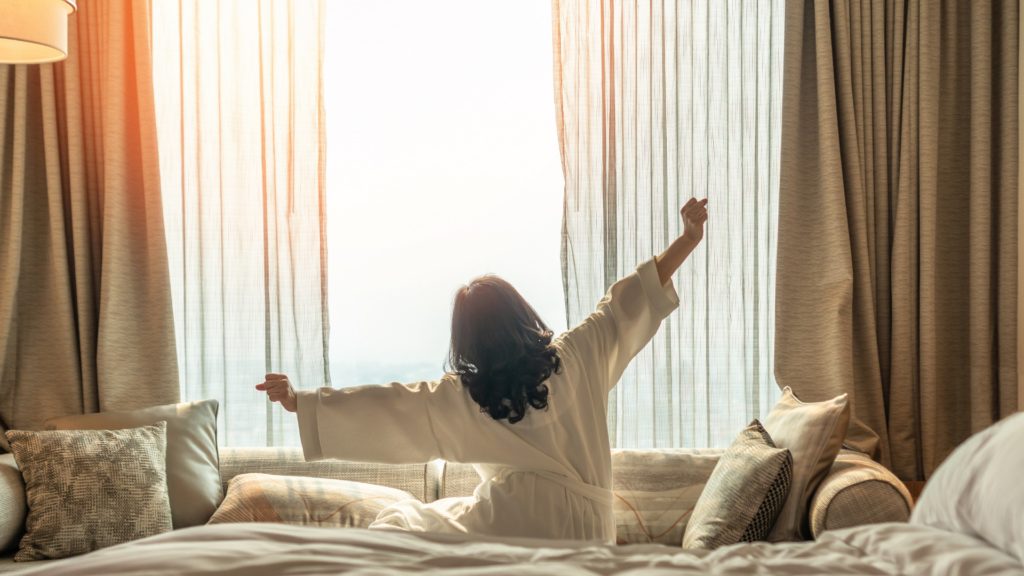 Frau sitzt auf dem Bett und streckt sich am Morgen ausgeschlafen