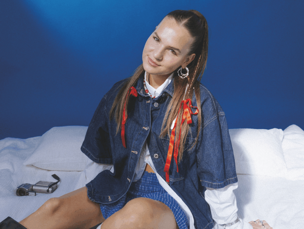 Sandra Hesch sitzt auf einem Bett vor blauem Hintergrund 
