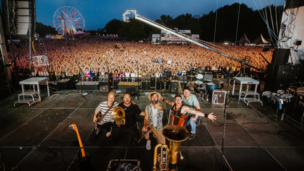 Die Band Fäaschtbänkler posiert auf der Bühne vor einer riesigen Festivalkulisse mit tausenden Besucherinnen und Besuchern bei einem der beliebtesten Events des Jahres.