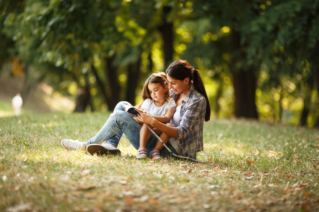 Mutter liest Tochter aus einem Buch in der Wiese vor.