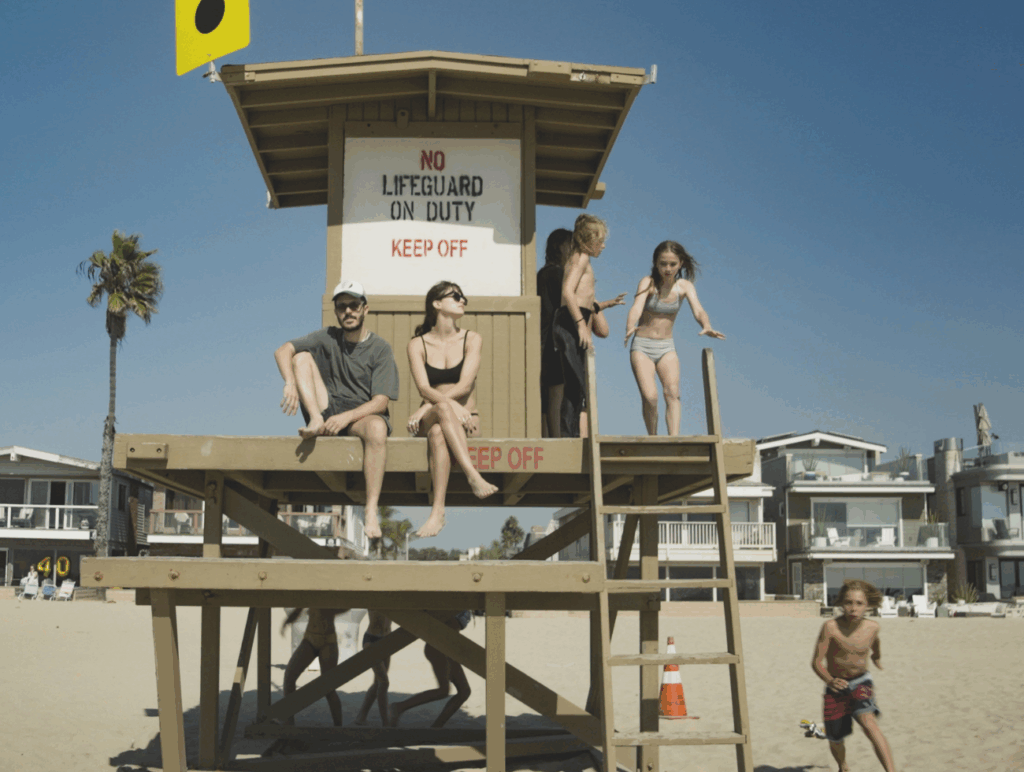 Filmszene aus "Noga", Menschen auf einer Lifeguard-Hütte auf einem Strand