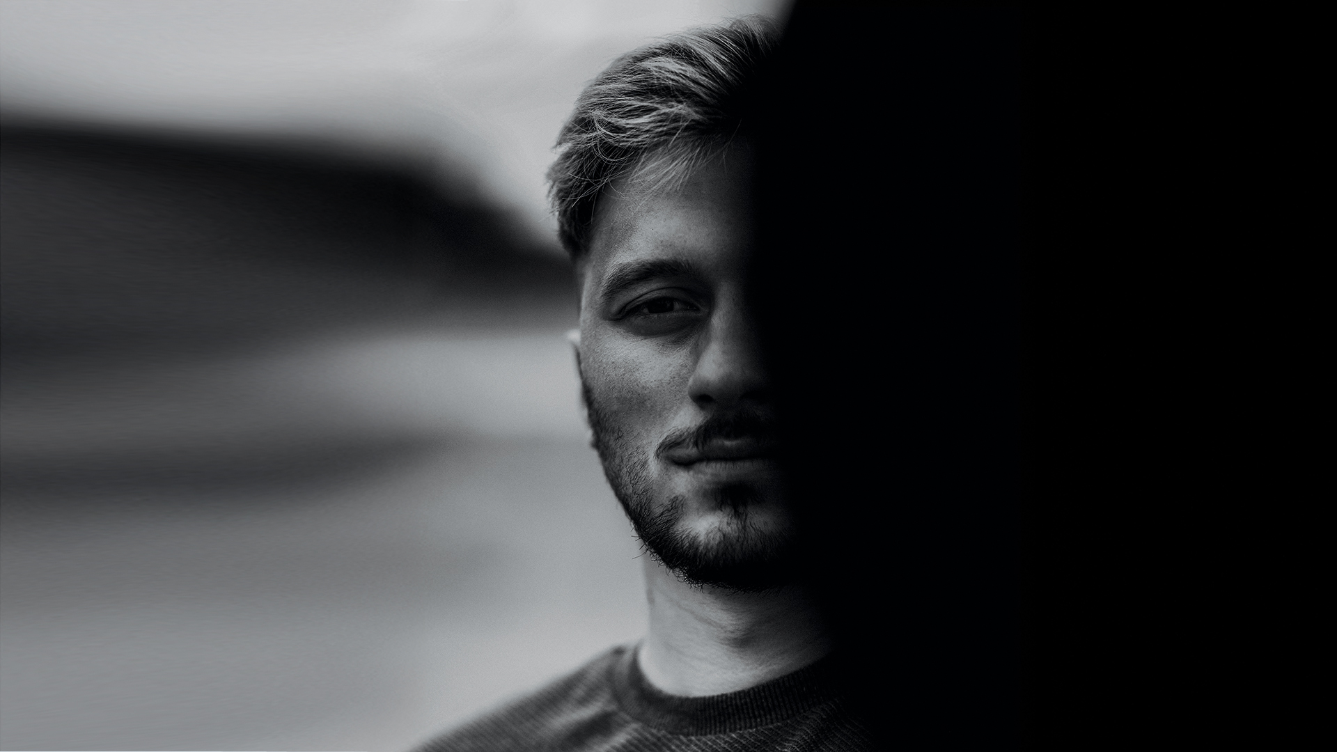 Femizid: Schwarz-Weiß-Porträt eines Mannes, dessen Gesicht zur Hälfte im Schatten liegt, als Symbolbild für Gewalt und Bedrohung.