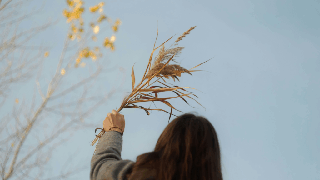 Eine Frau von hinten hält herbstblumen in den Himmel