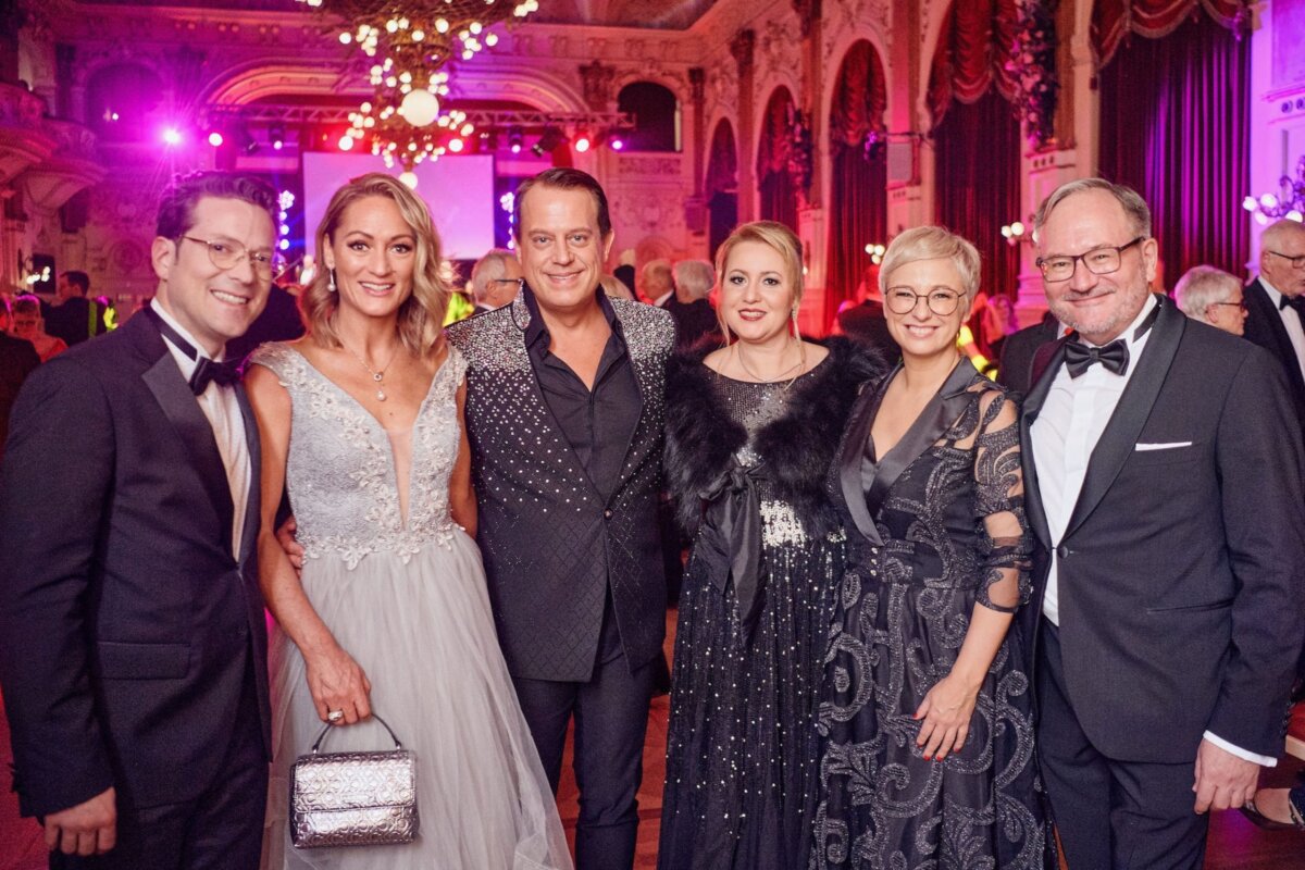 Sechs Frauen und MÃ¤nner in eleganter Kleidung im Ballsaal.