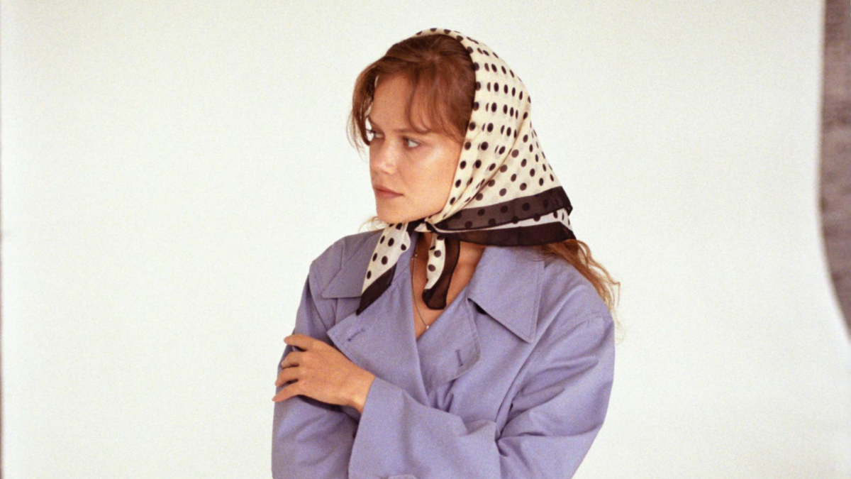 Polka Dots Trend 2025: Eine Frau mit Stirnfransen trÃ¤gt einen gepunkteten Schal als Kopftuch und dazu einen lila Trenchcoat.