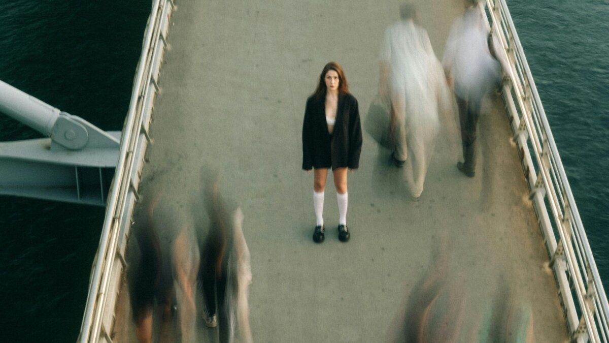 Frau steht auf einer BrÃ¼cke umgeben von Menschen, die an ihr vorbeigehen.